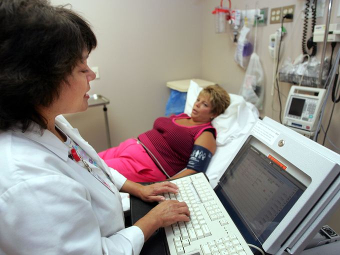 Cindy Owens, left, interim director of Hendersonville's Medical Center emergency room, uses a computer on wheels as she does a reassessment on Melinda Knowles of Hendersonville, who came in for back pain Aug. 16, 2005